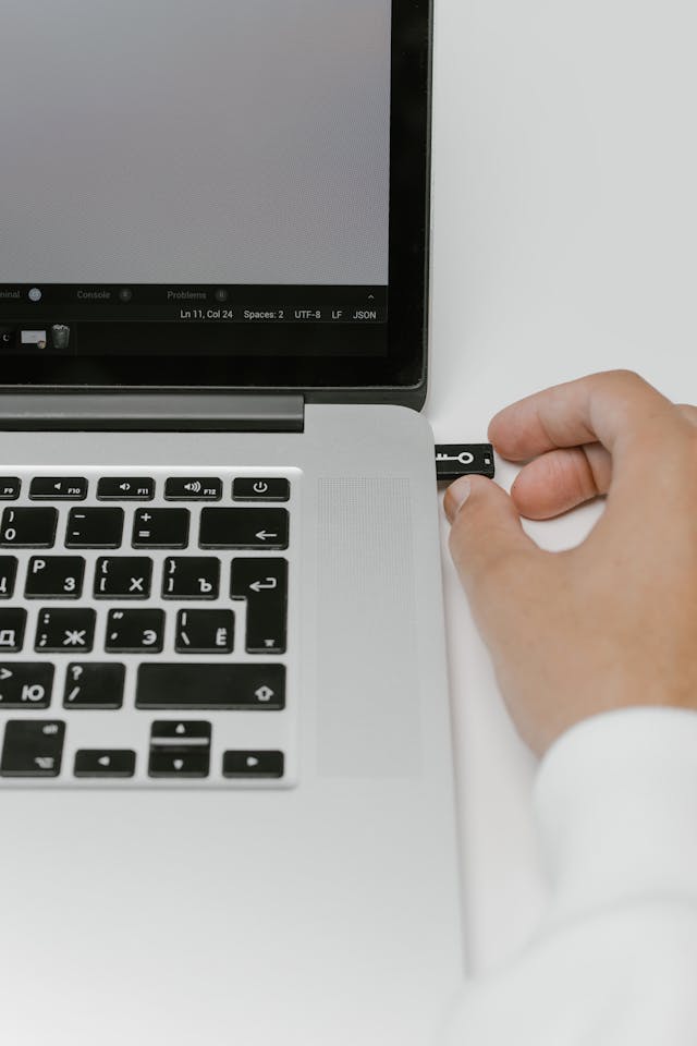 A person putting a USB flash drive in a silver laptop.