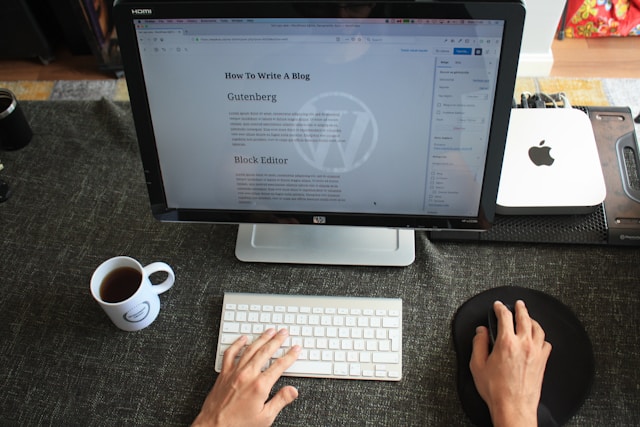 A person working on a live document in a spreadsheet on a laptop, with a notebook, sunglasses, and coffee on a wooden table.